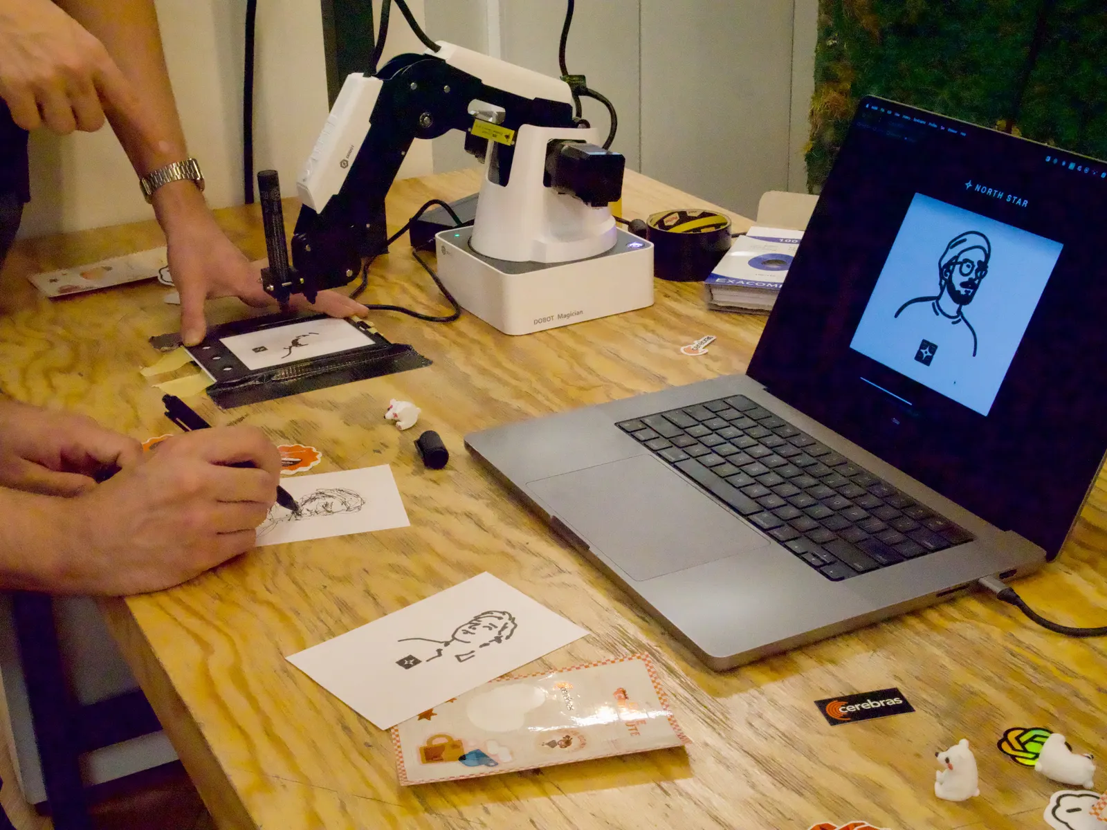 A person holding a card in place while the robot arm draws
