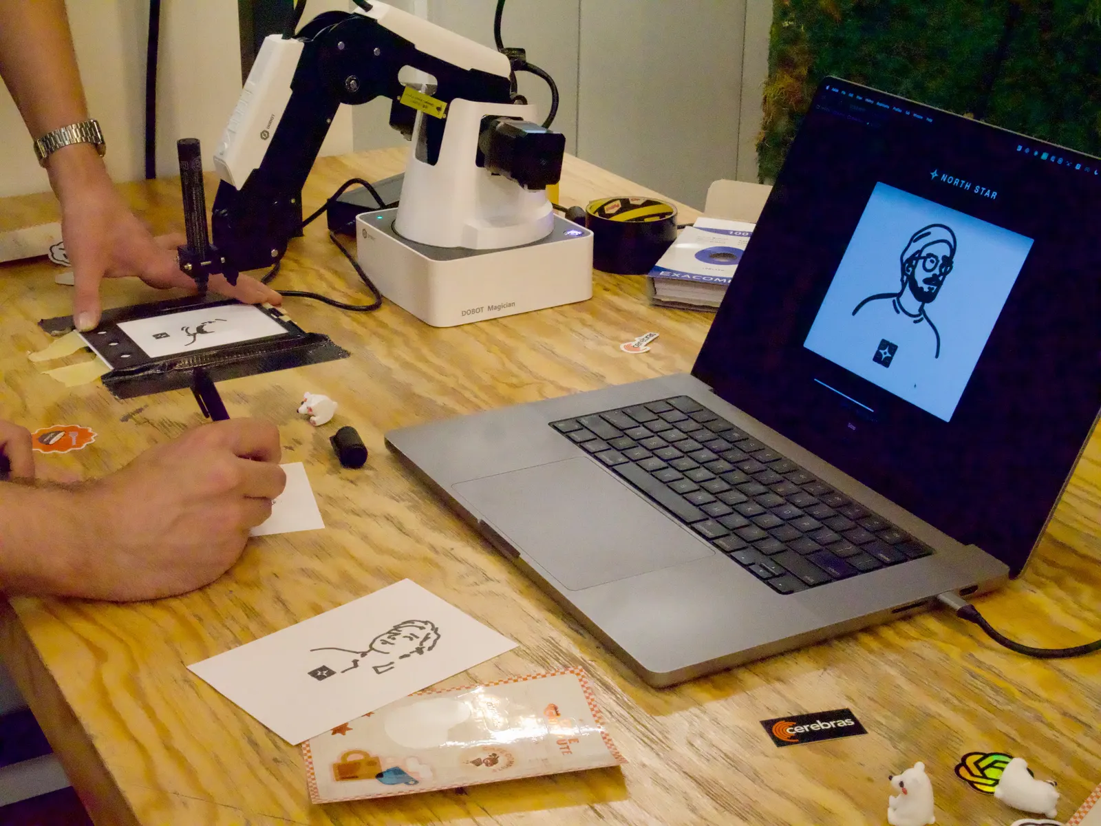 MARK-E drawing a portrait on a card, with the generated line art on a laptop beside it